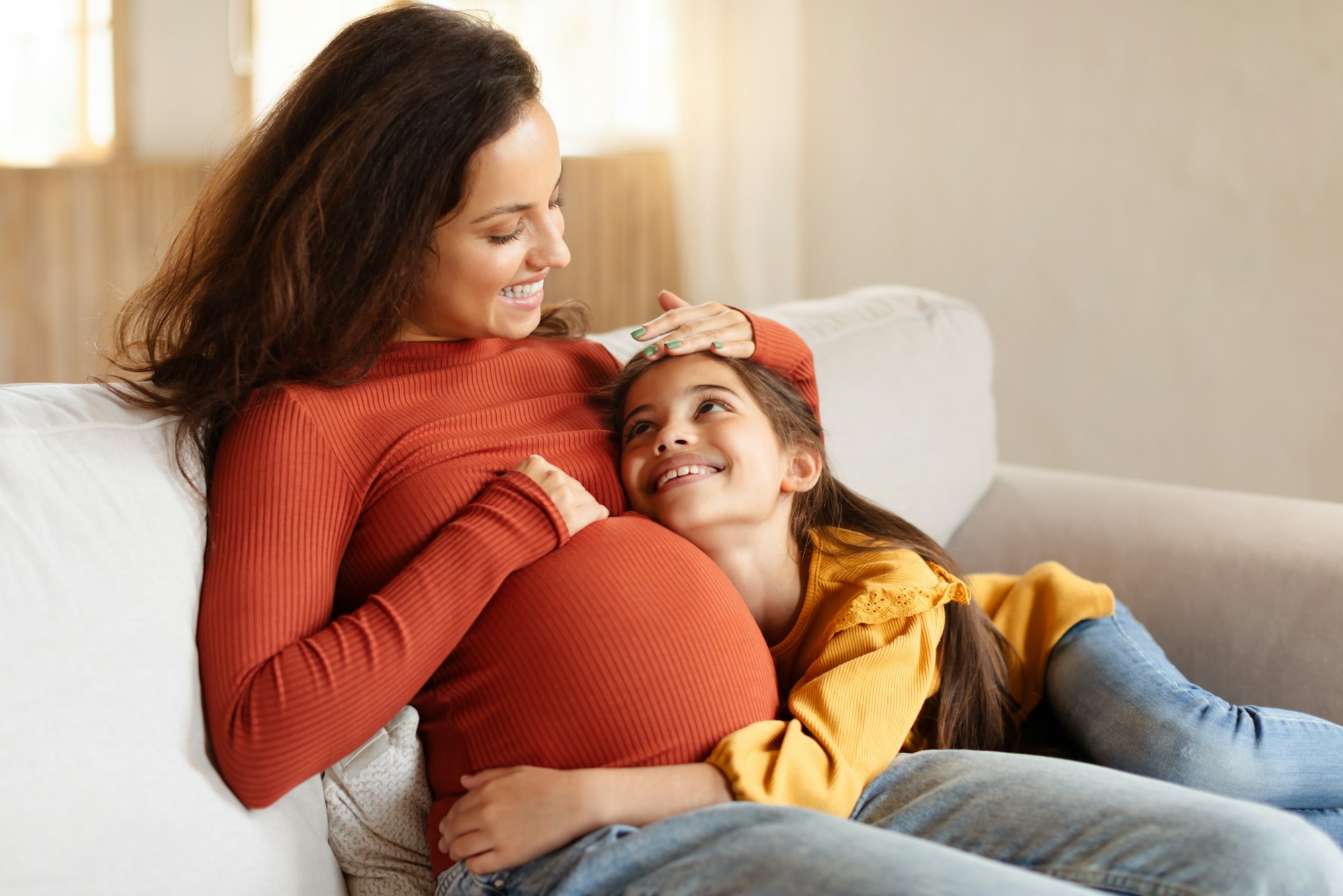 Kid girl touching her pregnant mother's belly at home