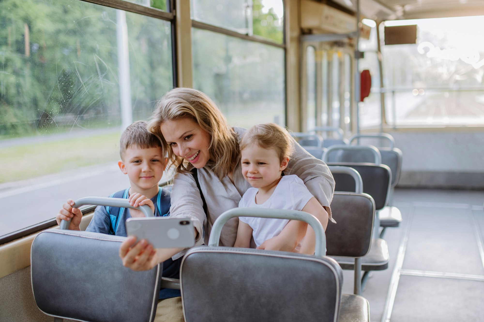 Young mother with little kids travelling in tram in summer and taking selfie.